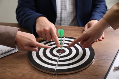 Business targeting concept. People pointing at dartboard at wooden table, closeup