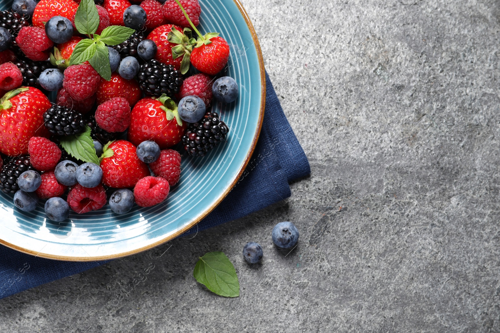 Photo of Many different fresh ripe berries in plate on grey table, flat lay. Space for text