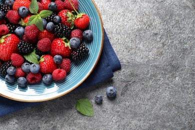 Many different fresh ripe berries in plate on grey table, flat lay. Space for text