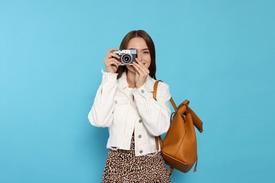 Young woman with camera taking photo on light blue background. Interesting hobby