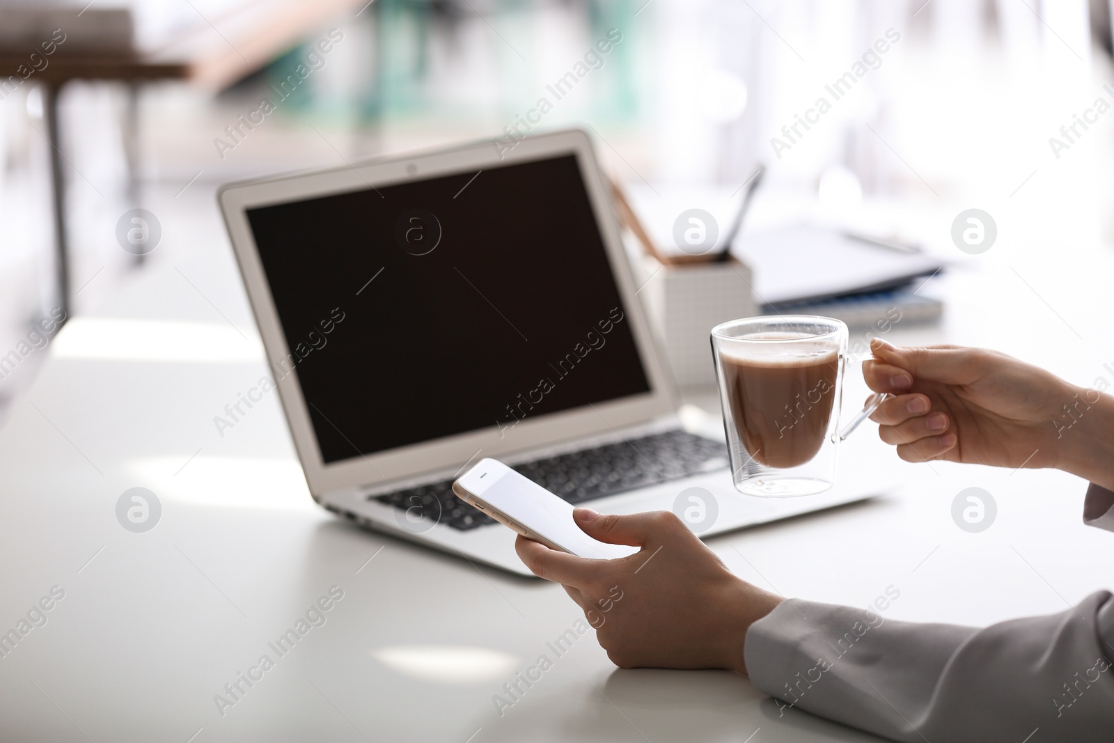Photo of Woman with cup of coffee, mobile phone and laptop at table, closeup