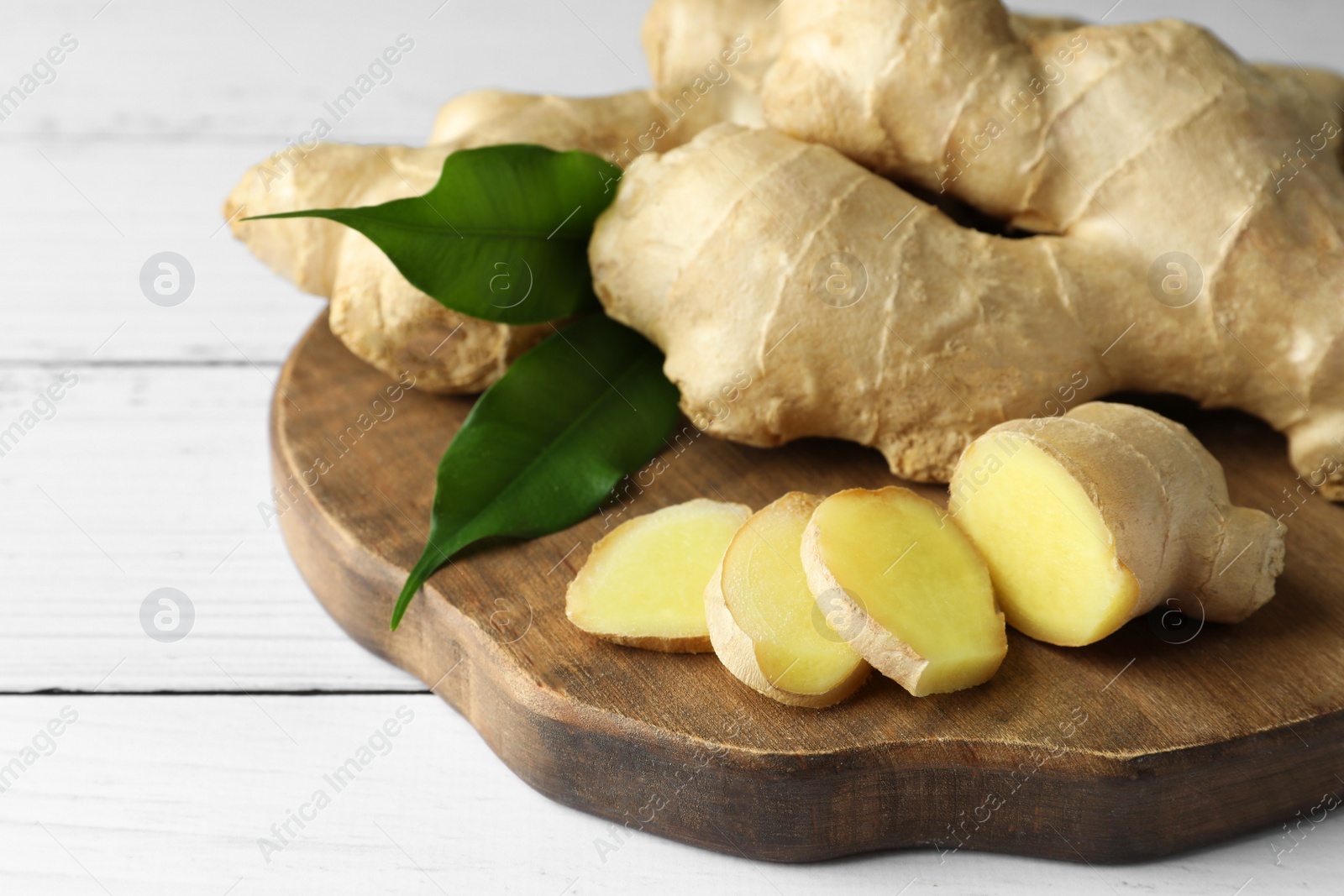 Photo of Cut and whole fresh ginger with leaves on white wooden table, closeup