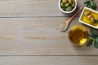 Photo of Fresh oil, ripe olives, dried herb and green leaves on wooden table, flat lay. Space for text