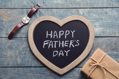 Gift box, watch and chalkboard with words HAPPY FATHER'S DAY on wooden background, top view