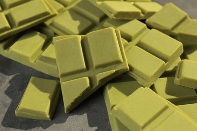 Photo of Pieces of tasty matcha chocolate bars on grey textured table, closeup