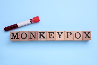 Word Monkeypox made of wooden cubes and test tube on light blue background, flat lay