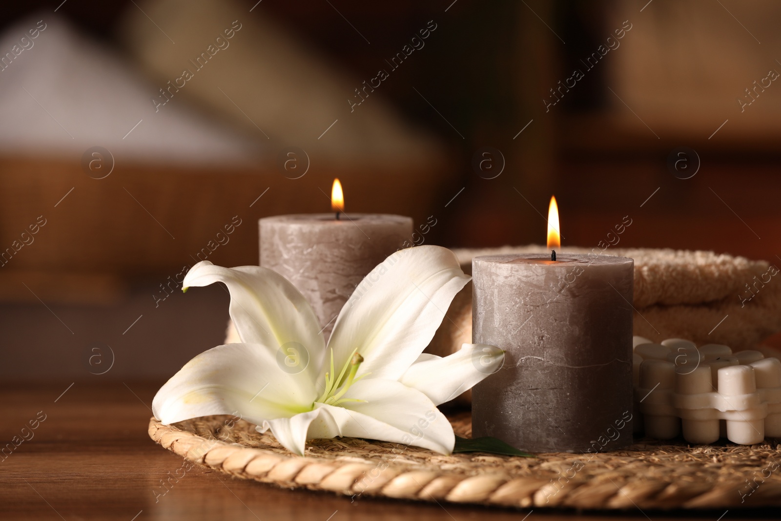 Photo of Spa composition with burning candles, lily flower and towels on wooden table in wellness center