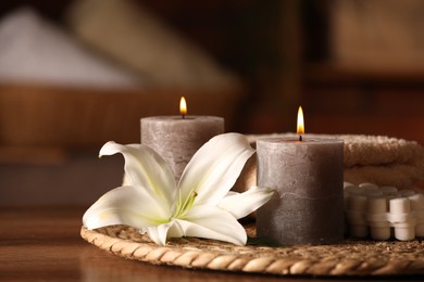 Photo of Spa composition with burning candles, lily flower and towels on wooden table in wellness center