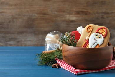 Photo of Tasty gingerbread cookies and fir branches on blue wooden table, space for text. St. Nicholas Day celebration