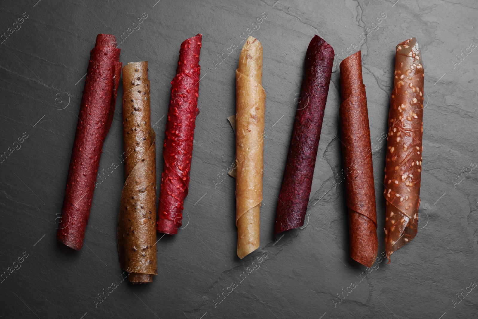 Photo of Delicious fruit leather rolls on black table, flat lay