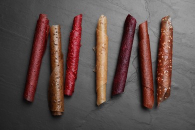 Photo of Delicious fruit leather rolls on black table, flat lay