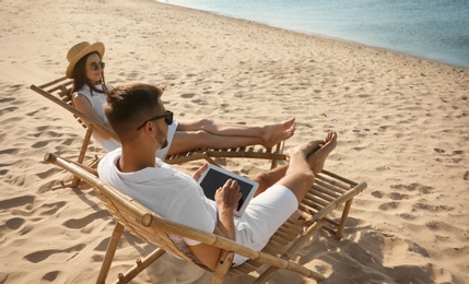 Photo of Young couple relaxing in deck chairs on sandy beach