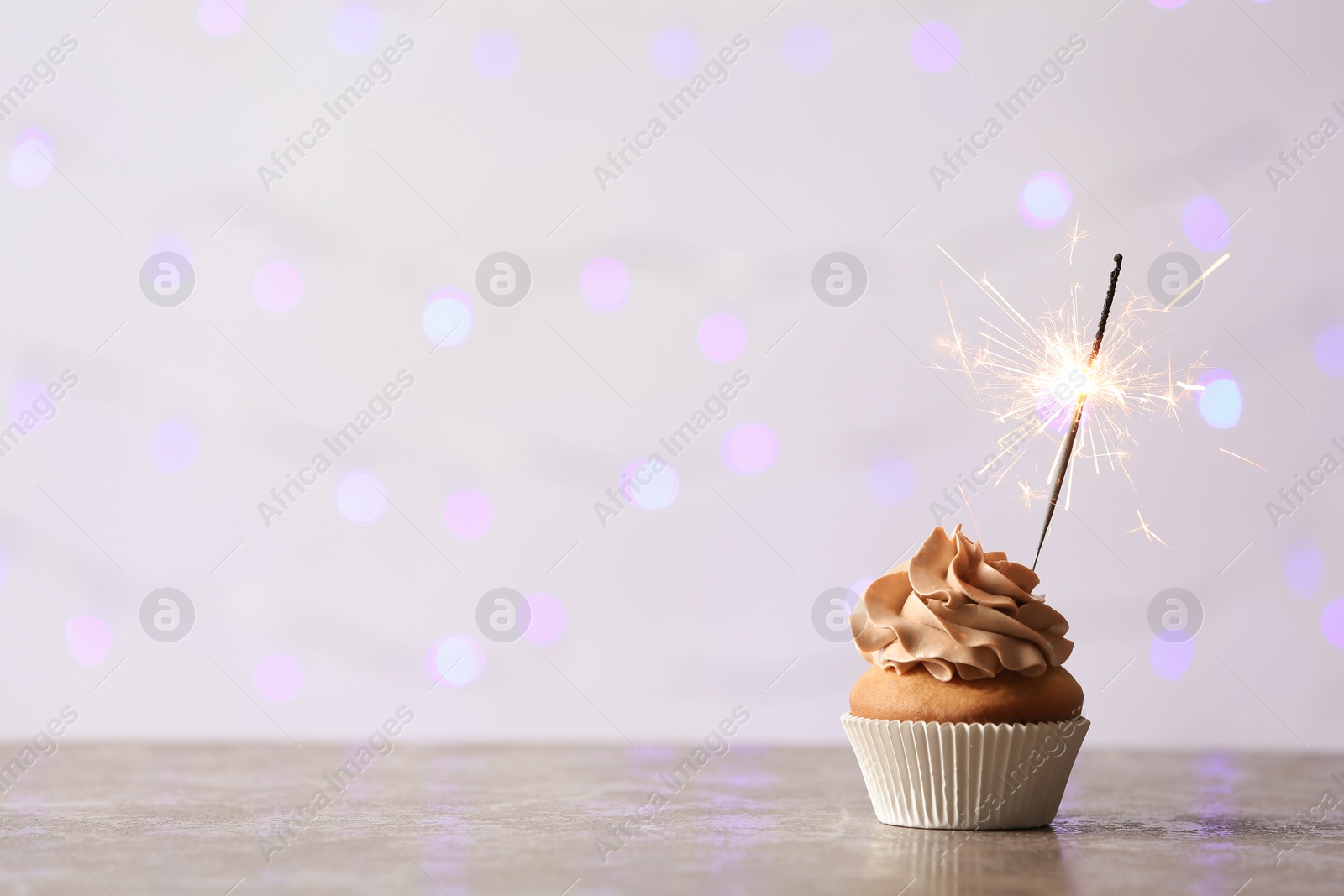 Photo of Delicious birthday cupcake with burning sparkler and space for text on blurred lights background