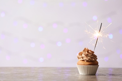 Photo of Delicious birthday cupcake with burning sparkler and space for text on blurred lights background