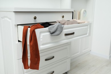 Photo of Cluttered chest of drawers indoors. Clothes in mess