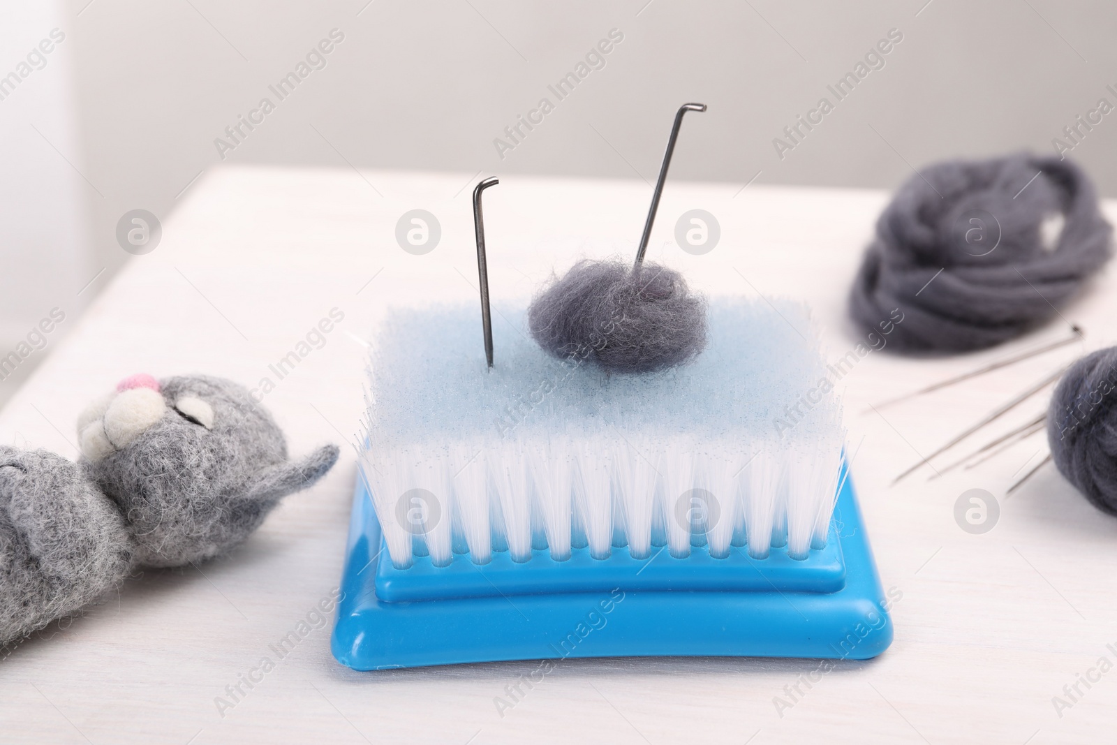 Photo of Felting tools, wool and toy cat on light wooden table, closeup