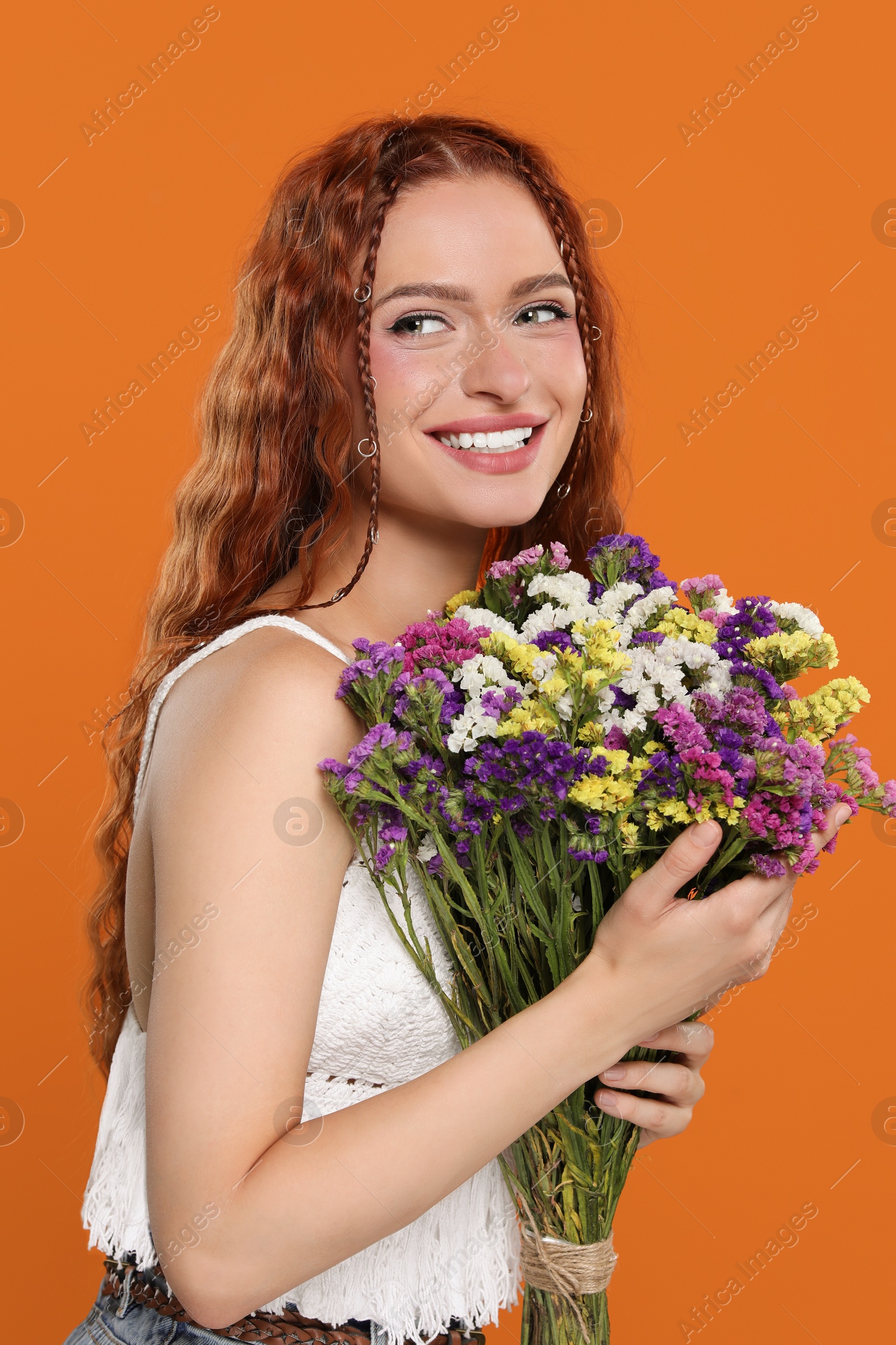 Photo of Beautiful young hippie woman with bouquet of colorful flowers on orange background