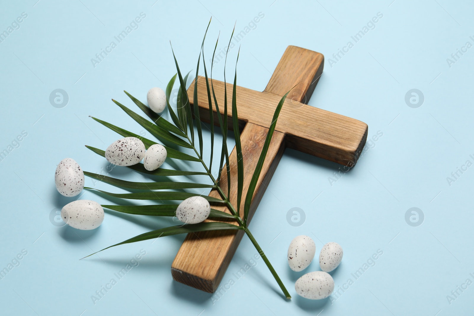 Photo of Wooden cross, painted Easter eggs and palm leaf on light blue background