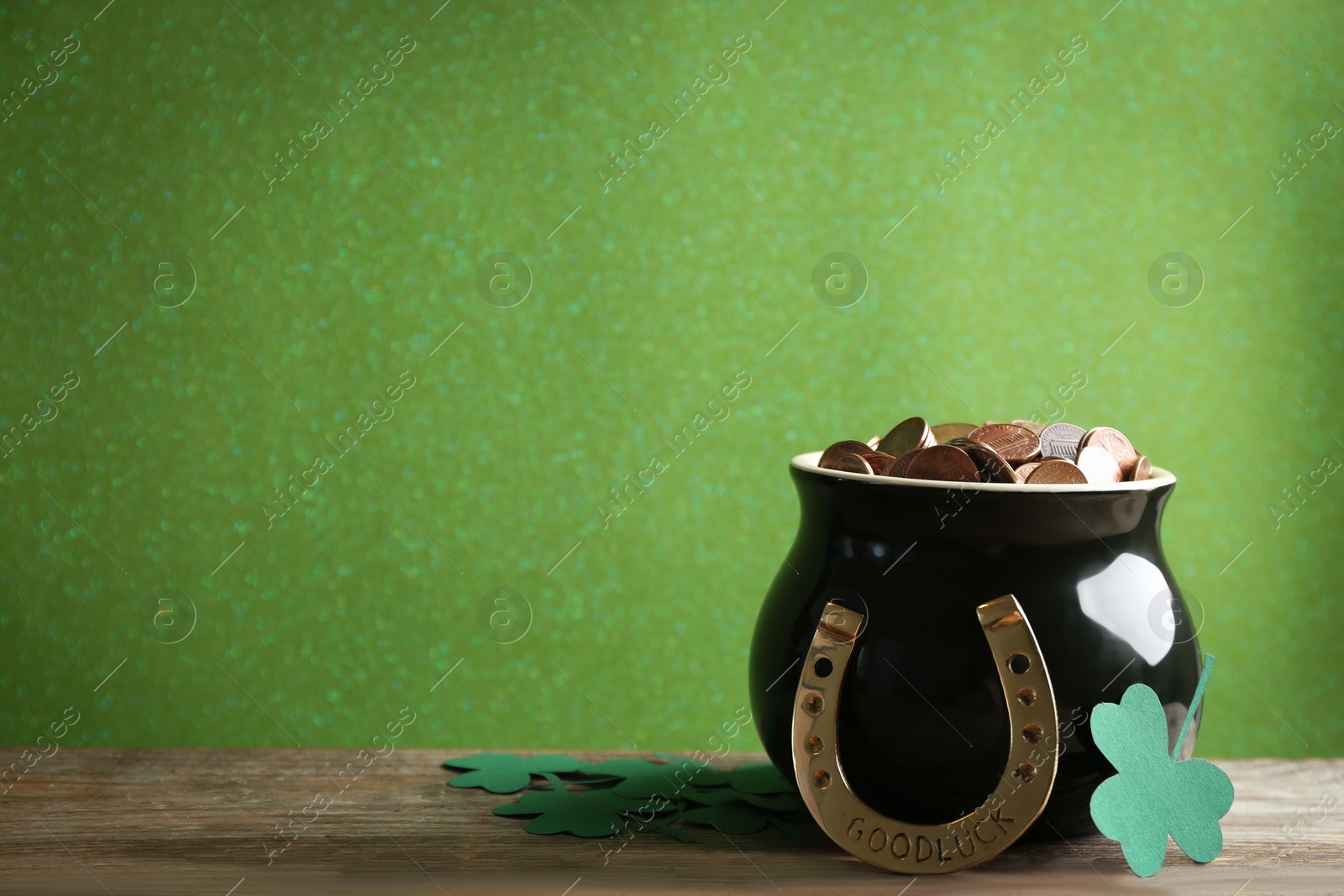 Photo of Pot of gold coins, horseshoe and clover leaves on wooden table against green background, space for text. St. Patrick's Day celebration