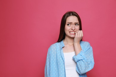 Photo of Young woman biting her nails on pink background. Space for text