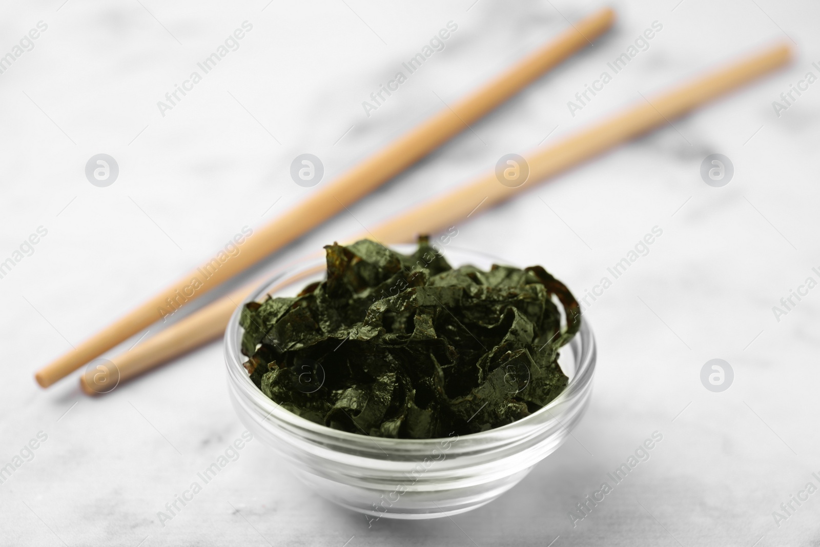 Photo of Chopped nori sheets with chopsticks on white marble table, closeup