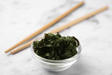 Photo of Chopped nori sheets with chopsticks on white marble table, closeup