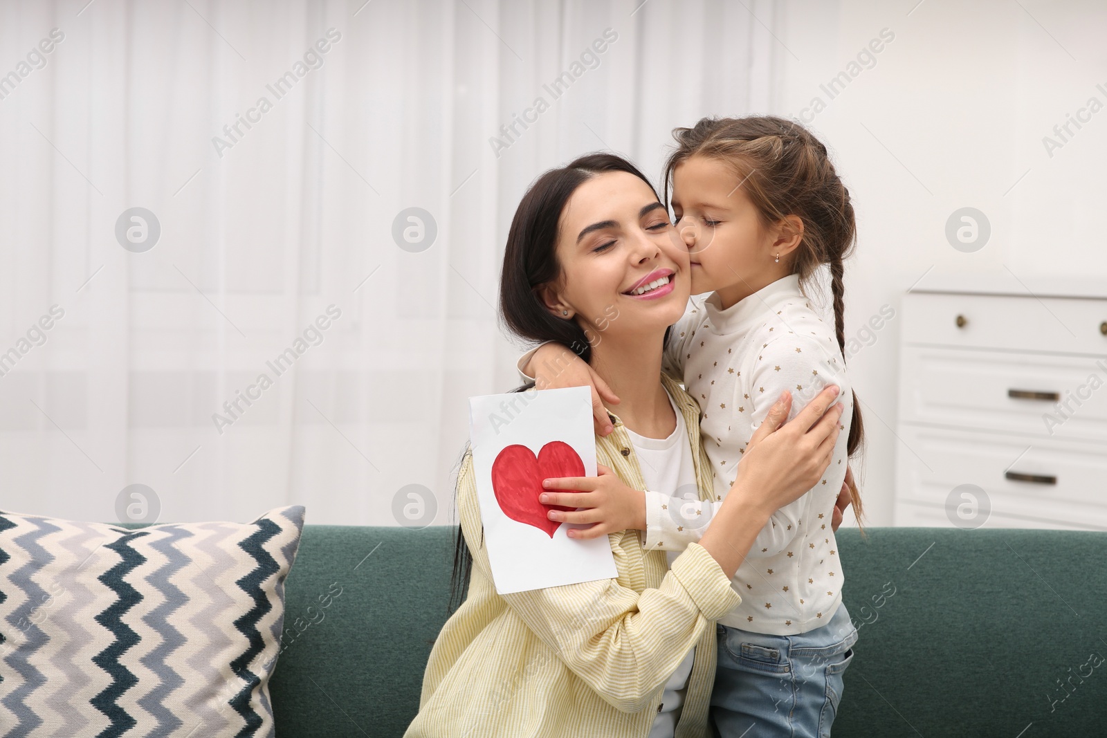 Photo of Happy woman with her daughter and handmade greeting card on sofa at home, space for text. Mother's day celebration
