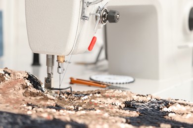 Photo of Sewing machine and beautiful fabric with paillettes indoors, closeup