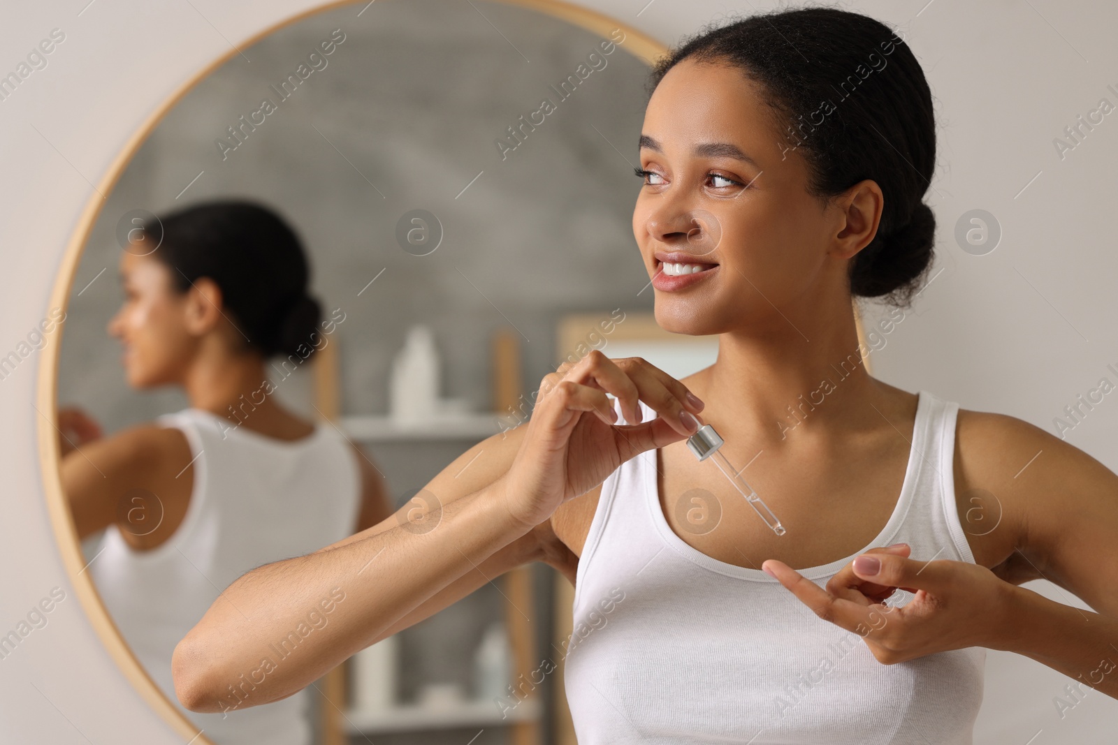 Photo of Smiling woman applying serum onto her finger in bathroom. Space for text