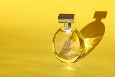 Luxury women's perfume. Sunlit glass bottle on yellow background. Space for text