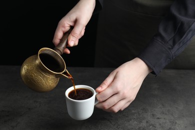 Photo of Turkish coffee. Woman pouring brewed beverage from cezve into cup at grey table, closeup