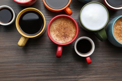 Many different cups with aromatic hot coffee on wooden table, flat lay