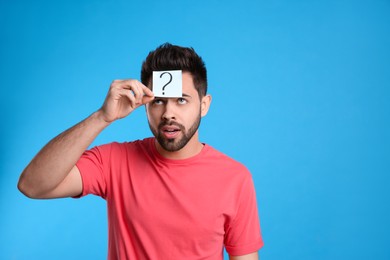 Emotional young man with question mark sticker on forehead against light blue background. Space for text