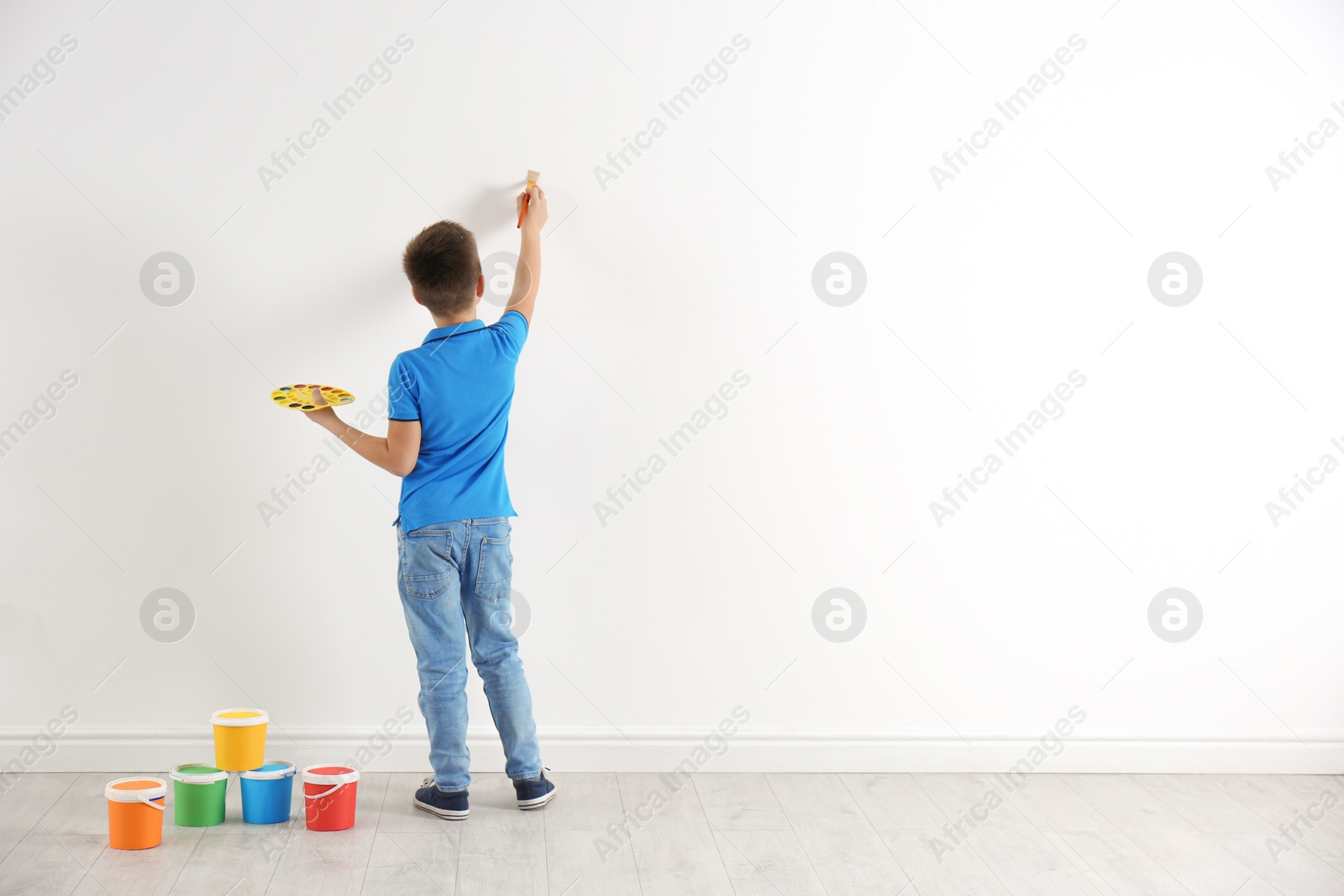 Photo of Little child painting on white wall indoors. Space for text