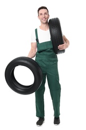 Photo of Young mechanic in uniform holding car tires on white background