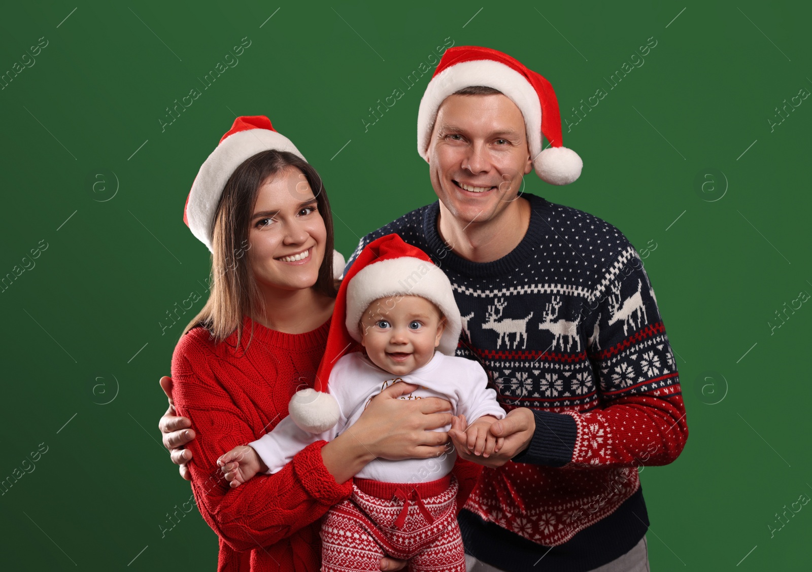 Photo of Happy couple with cute baby in Christmas outfits and Santa hats on green background