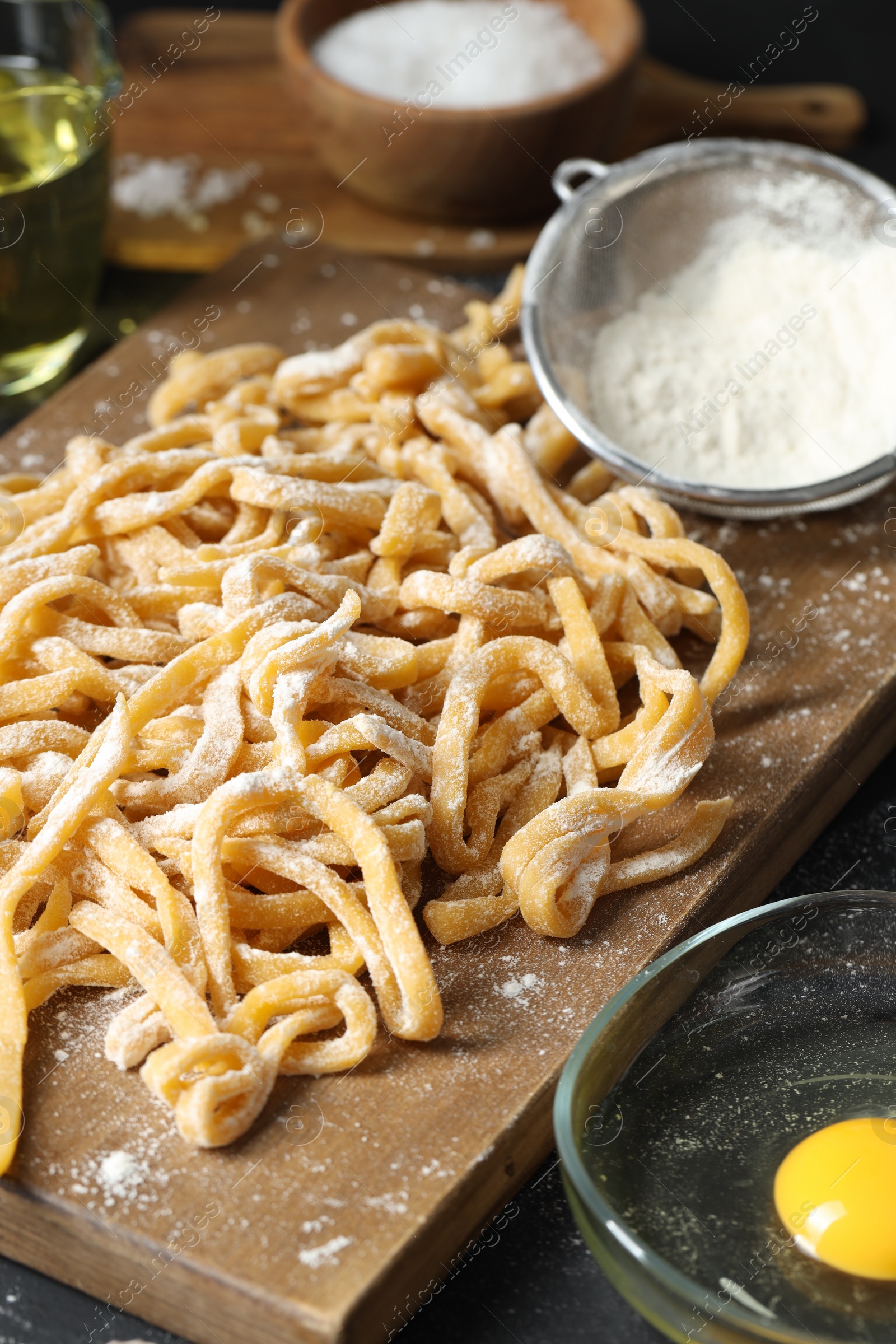 Photo of Board with homemade pasta, flour and ingredients on dark table