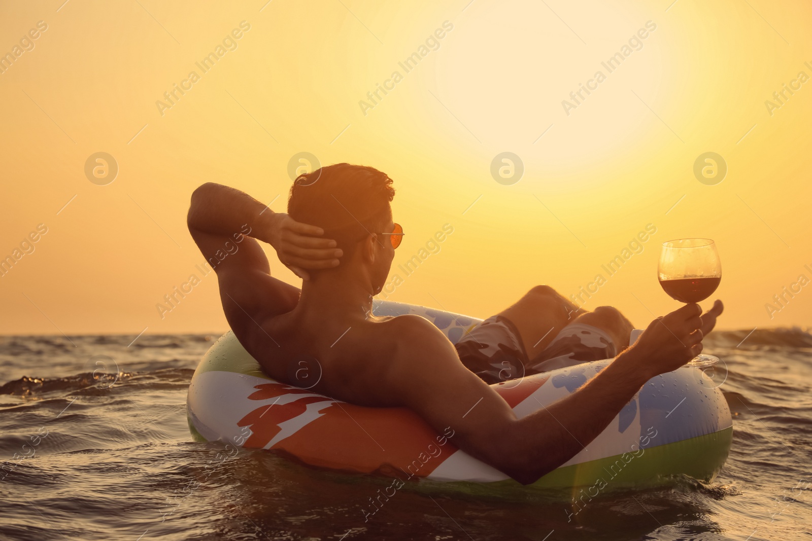 Photo of Man with glass of wine and inflatable ring in sea at sunset