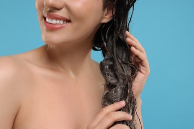 Smiling woman washing hair on light blue background, closeup