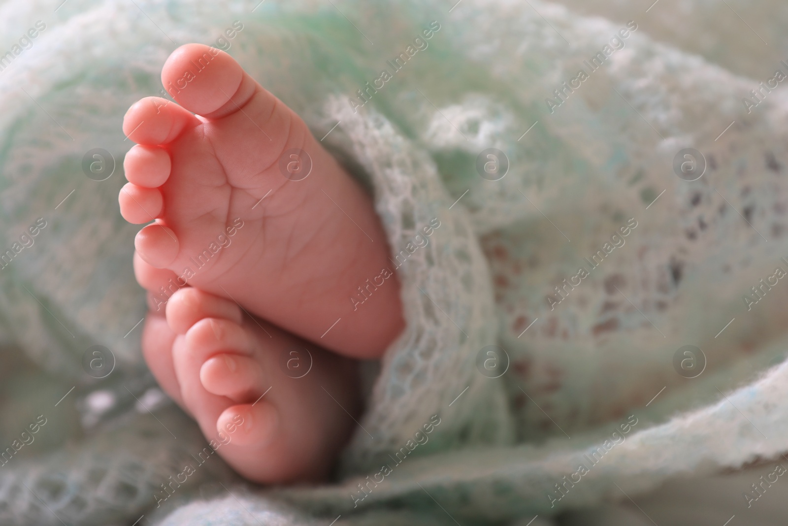 Photo of Cute newborn baby covered in turquoise crocheted plaid on bed, closeup of legs