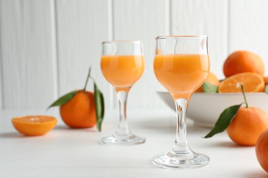 Photo of Tasty tangerine liqueur in glasses and fresh fruits on white table. Space for text