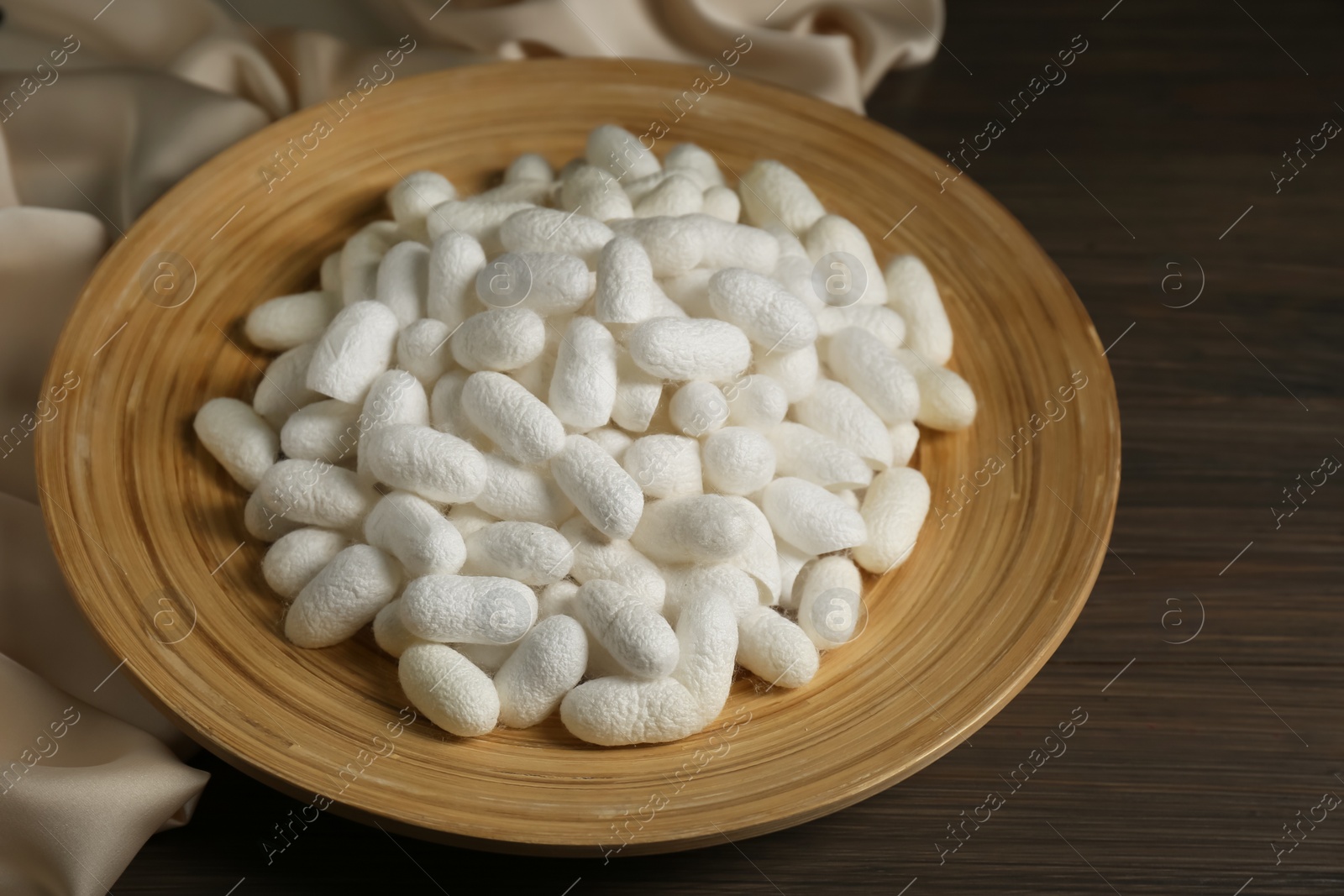 Photo of White cocoons with plate and silk fabric on wooden table