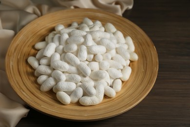 White cocoons with plate and silk fabric on wooden table