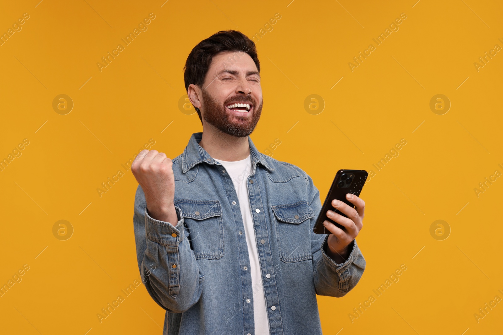 Photo of Happy man with smartphone on orange background