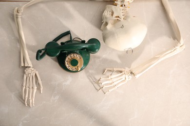 Photo of Waiting concept. Human skeleton at grey marble table with corded telephone, top view