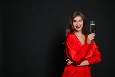 Photo of Happy woman with glass of champagne on black background, space for text. Christmas party