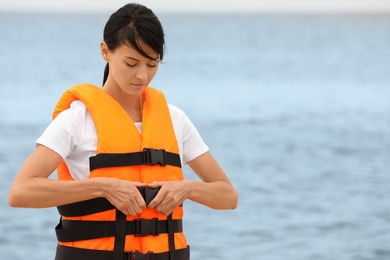 Photo of Beautiful female lifeguard putting on life vest near sea