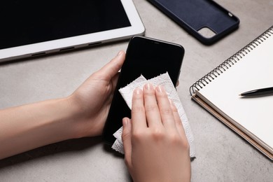 Photo of Woman wiping smartphone with paper towel at gray table, closeup