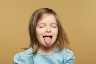 Photo of Funny little girl showing her tongue on beige background