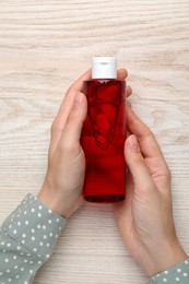 Photo of Woman holding micellar water in bottle at wooden table, top view